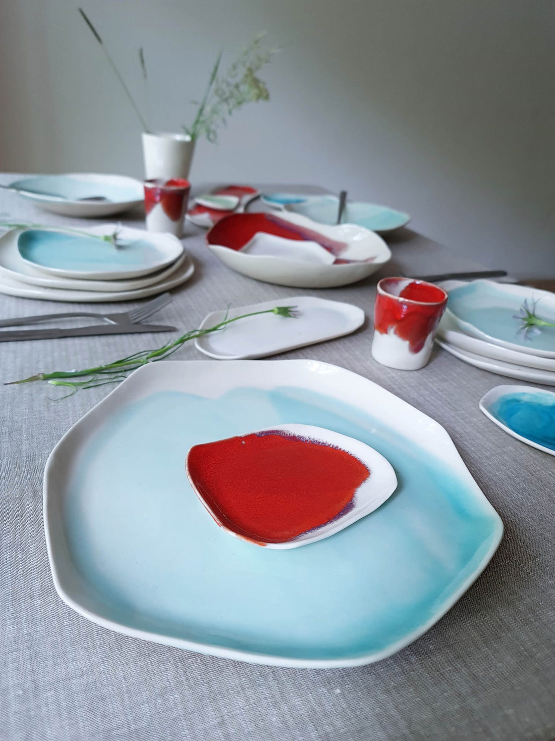 Table set with Turquoise porcelain plates and a small red dish on a grey linen cloth