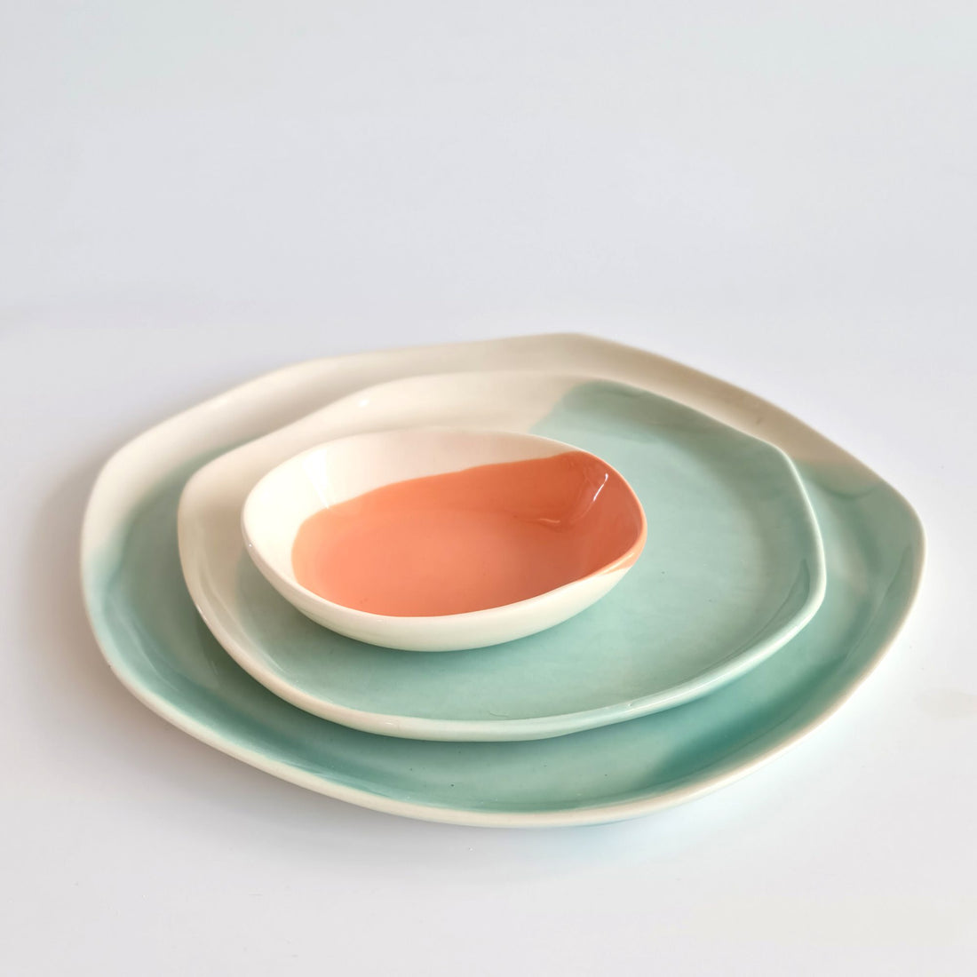 Turquoise handmade porcelain plates stacked with a small coral-glazed ceramic bowl