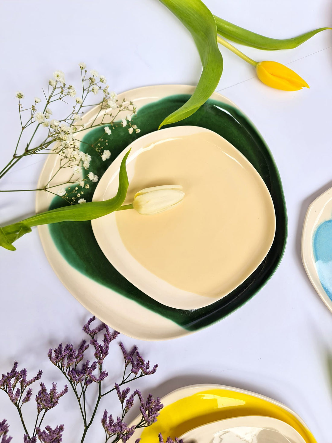 Ivory porcelain plate set on a dark green glazed plate with tulips and gypsophila