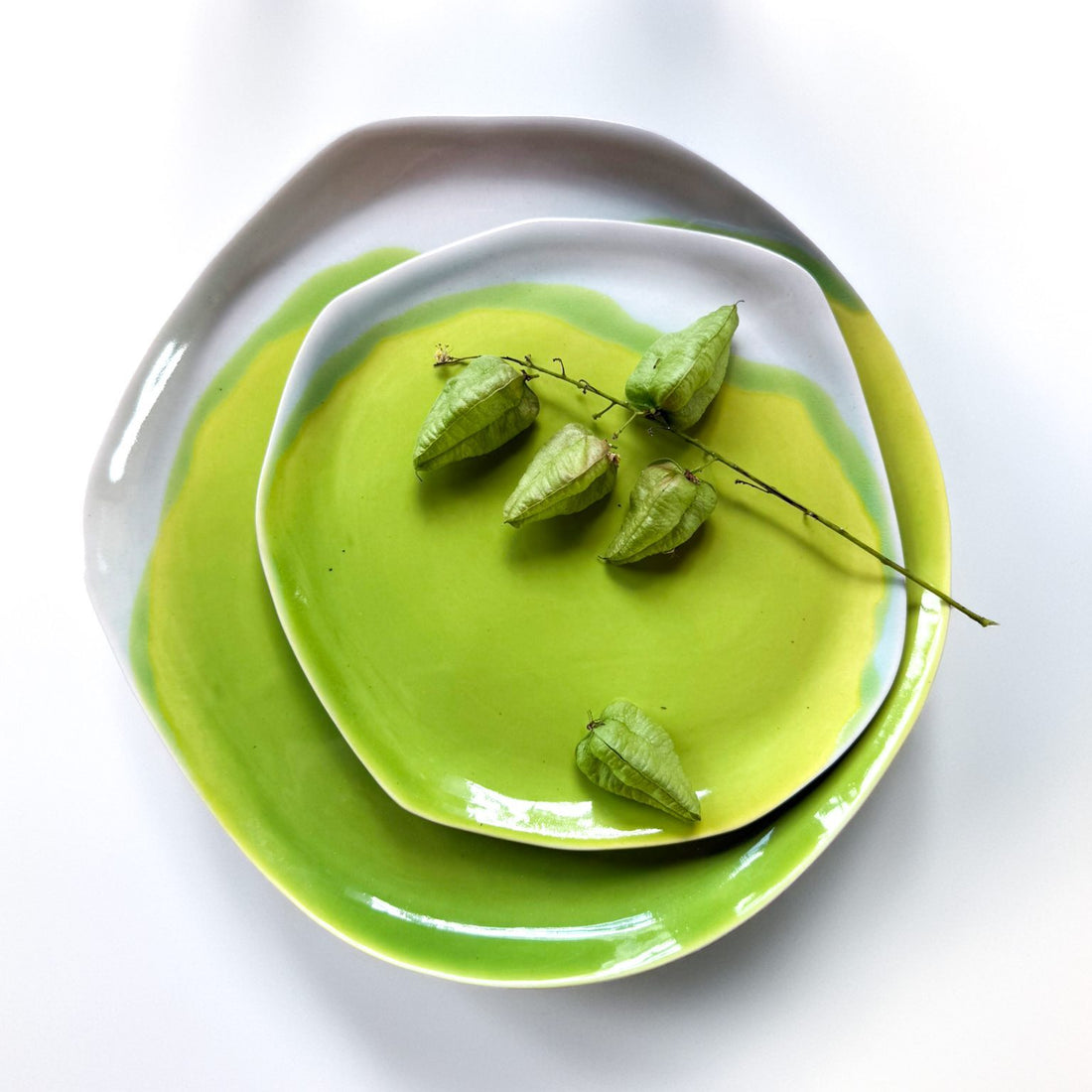 Stacked handmade porcelain plates in Electric Matcha glaze with white rims and dried physalis pods