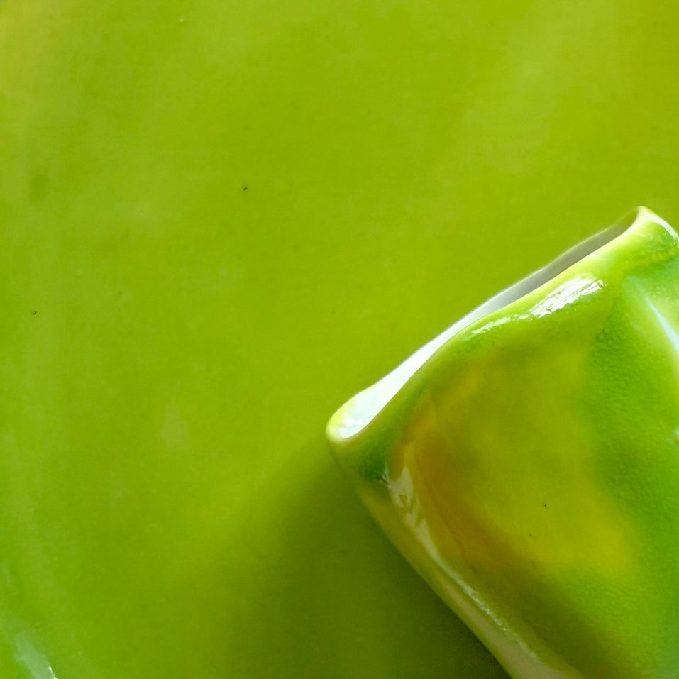Electric Matcha glossy glaze sample on handmade porcelain, with the edge of a bright green cup
