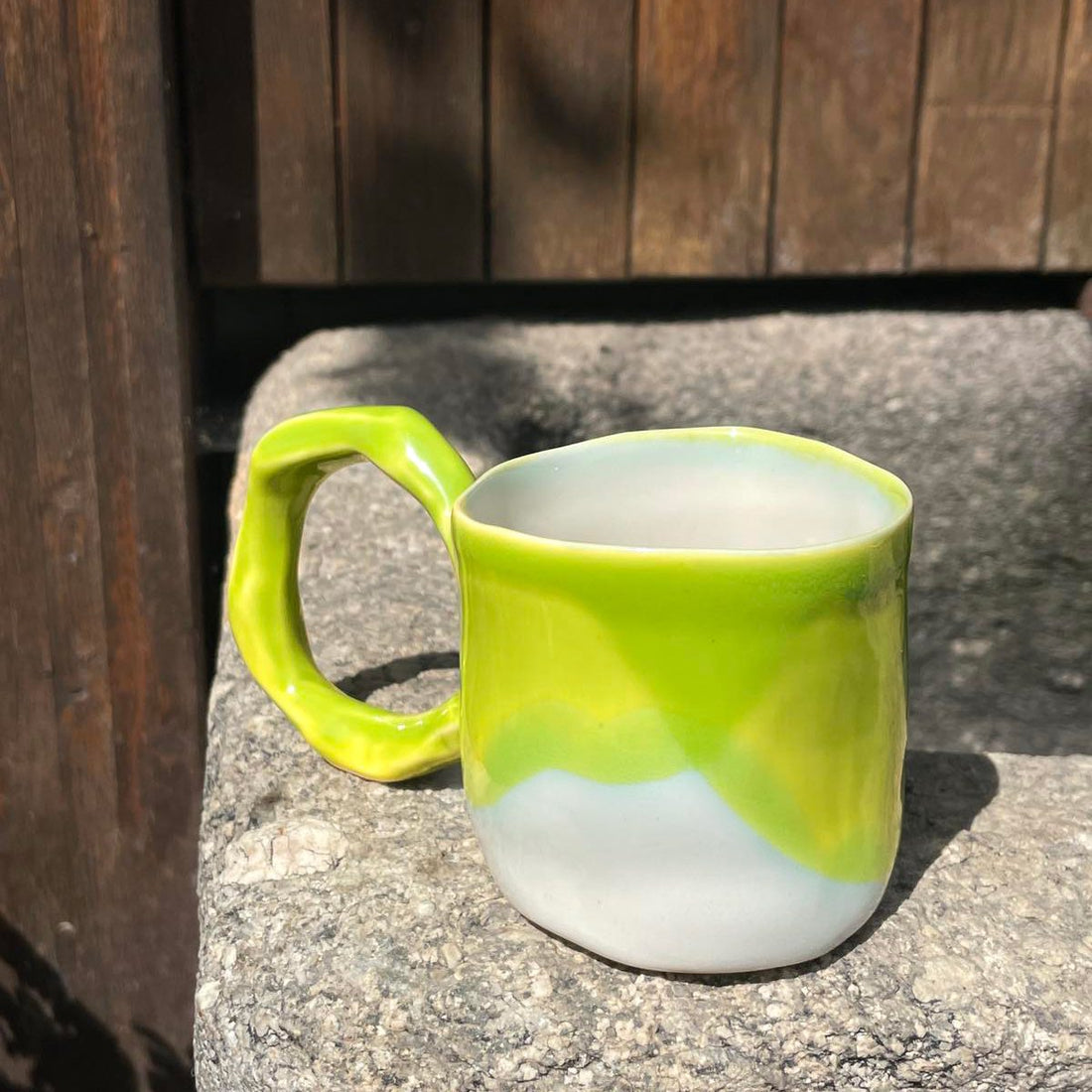 Handmade porcelain mug in Lime glaze over white, with a sculpted handle, on a stone step outdoors