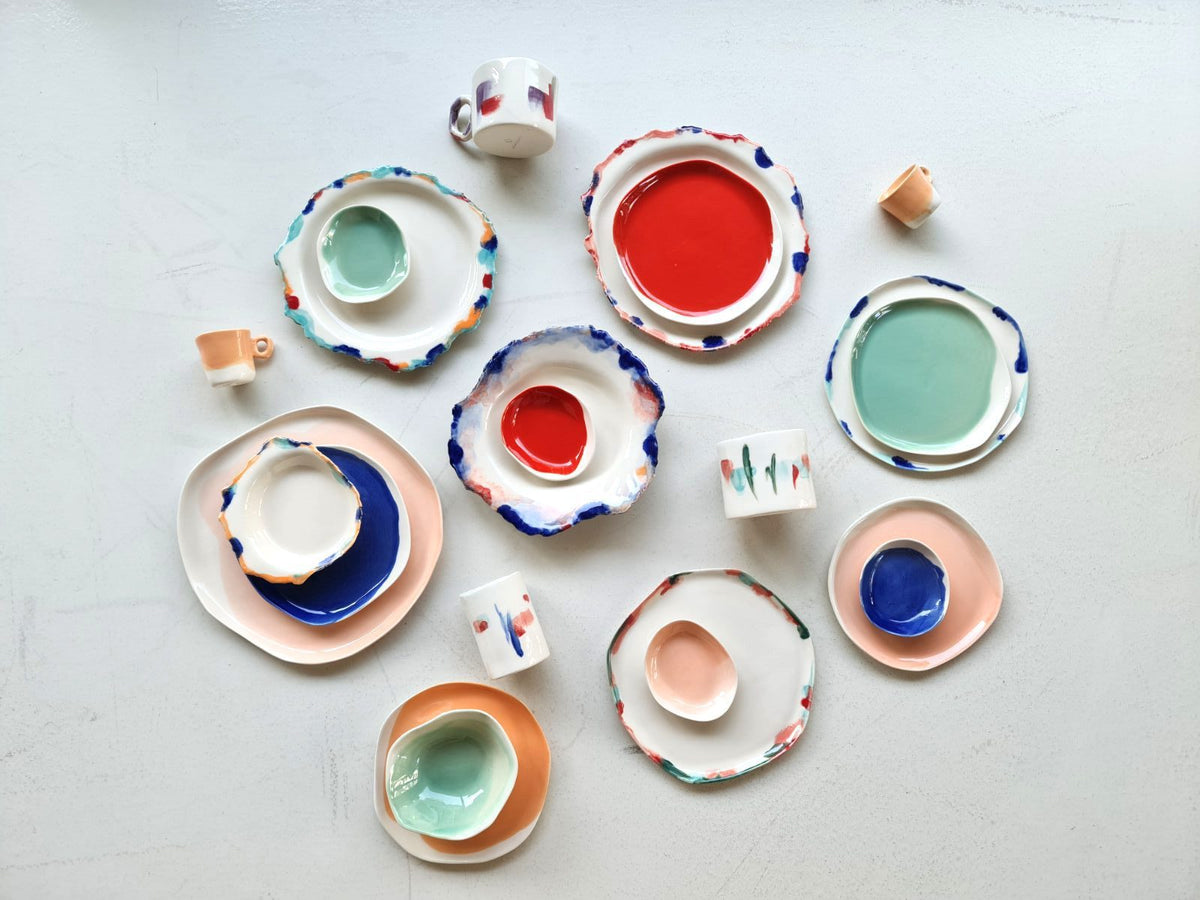 Color collection handmade porcelain plates, bowls and cups in red, blue and mint laid out on white