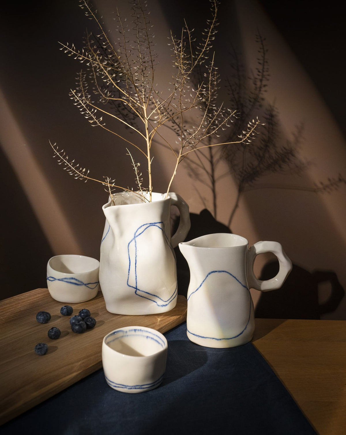 Ivory handmade ceramic jugs and cups with dried flowers on a dark table