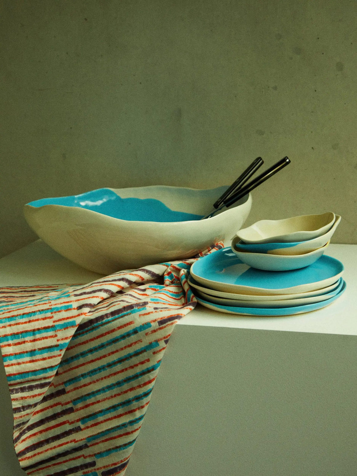 Turquoise and ivory ceramic bowls and plates on striped fabric