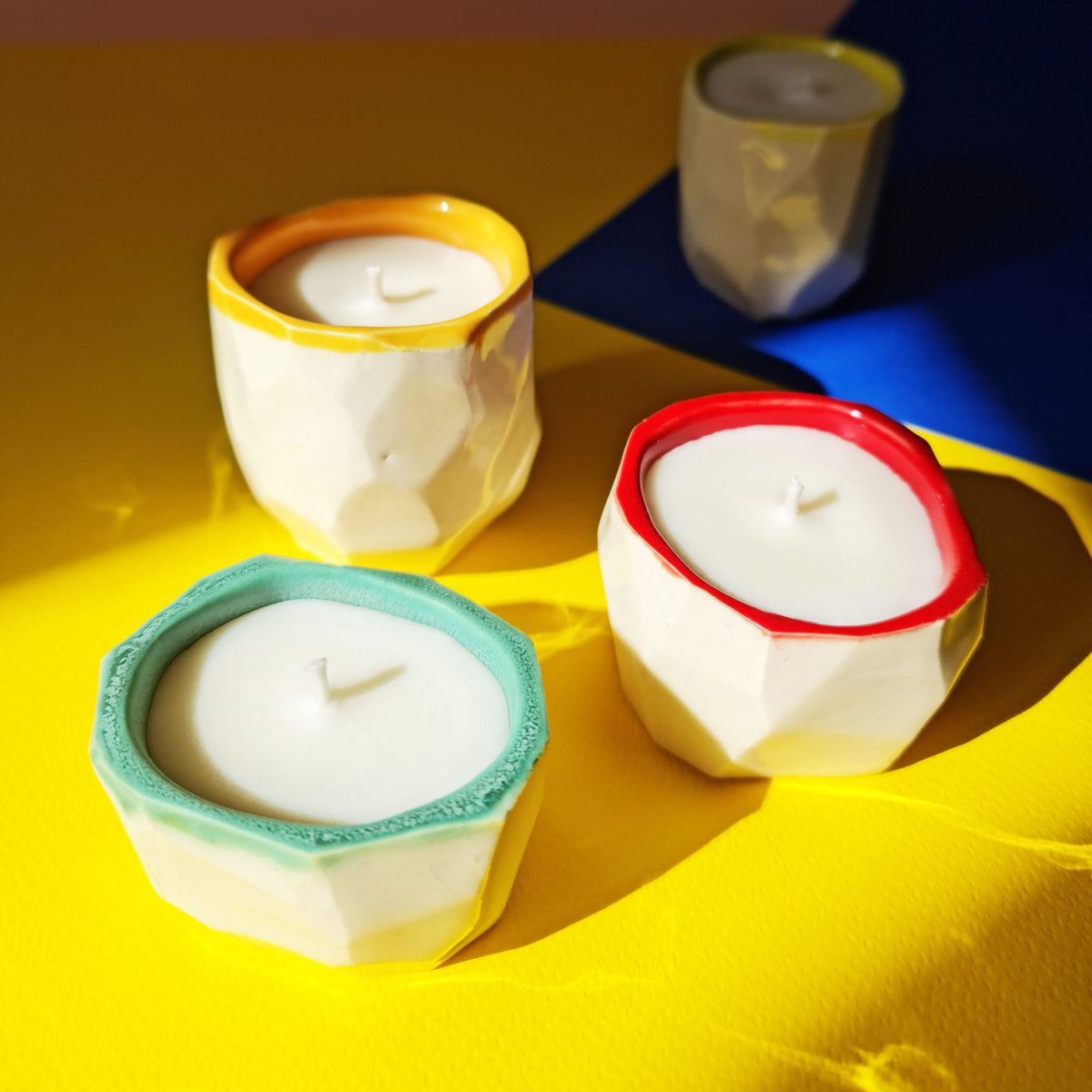 Faceted porcelain candle holders with yellow, red and turquoise glazed rims on a bright yellow table
