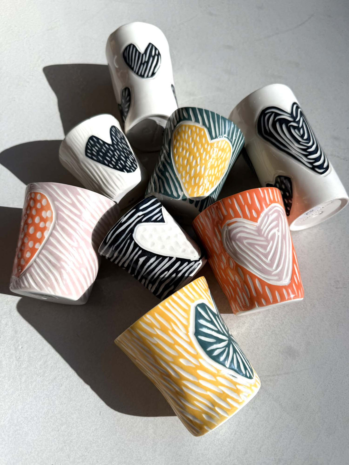 Sgraffito porcelain cups with carved heart motifs in black, pink and yellow for corporate gifts