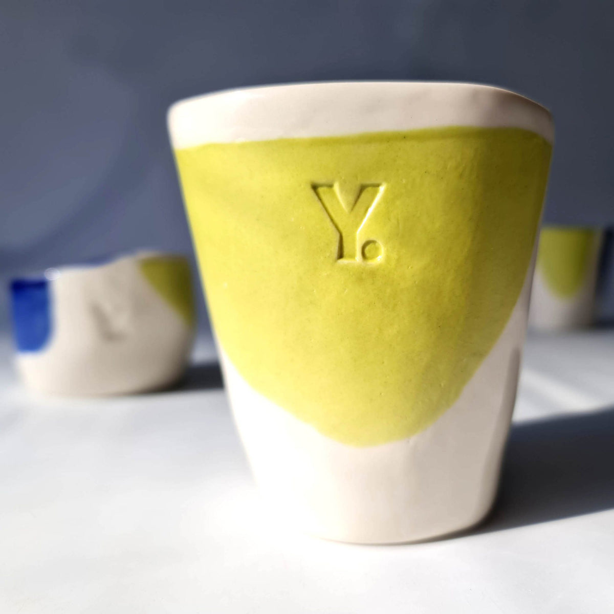 Yellow-and-ivory handmade ceramic cup with an embossed corporate logo