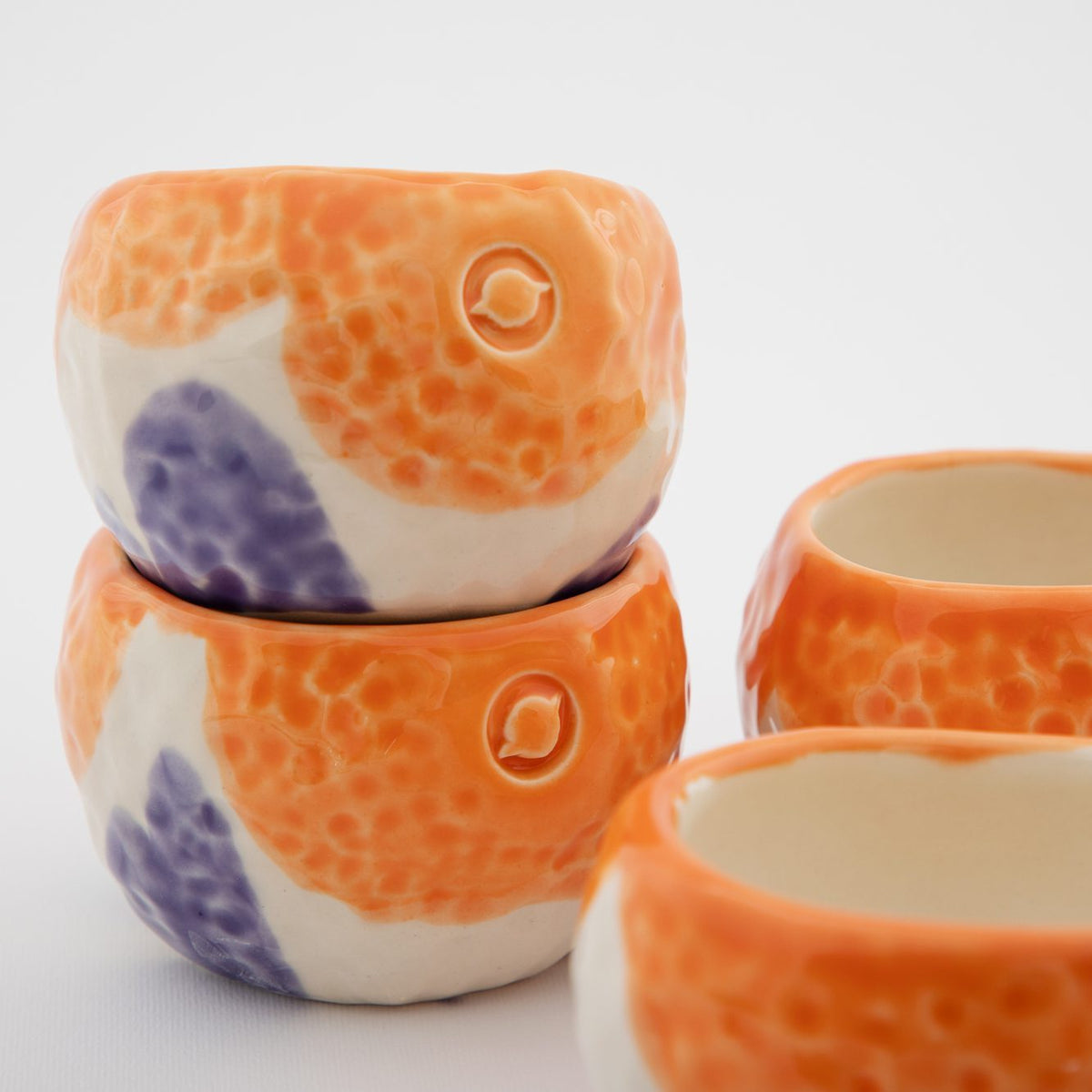 Orange and purple handmade ceramic cups with circular embossed logos
