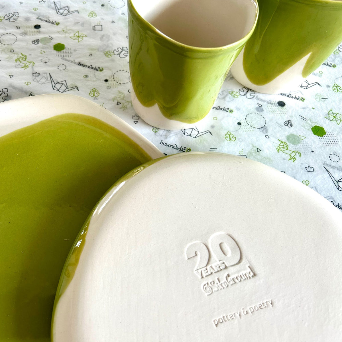 Green ceramic cups and an ivory plate with a relief corporate logo