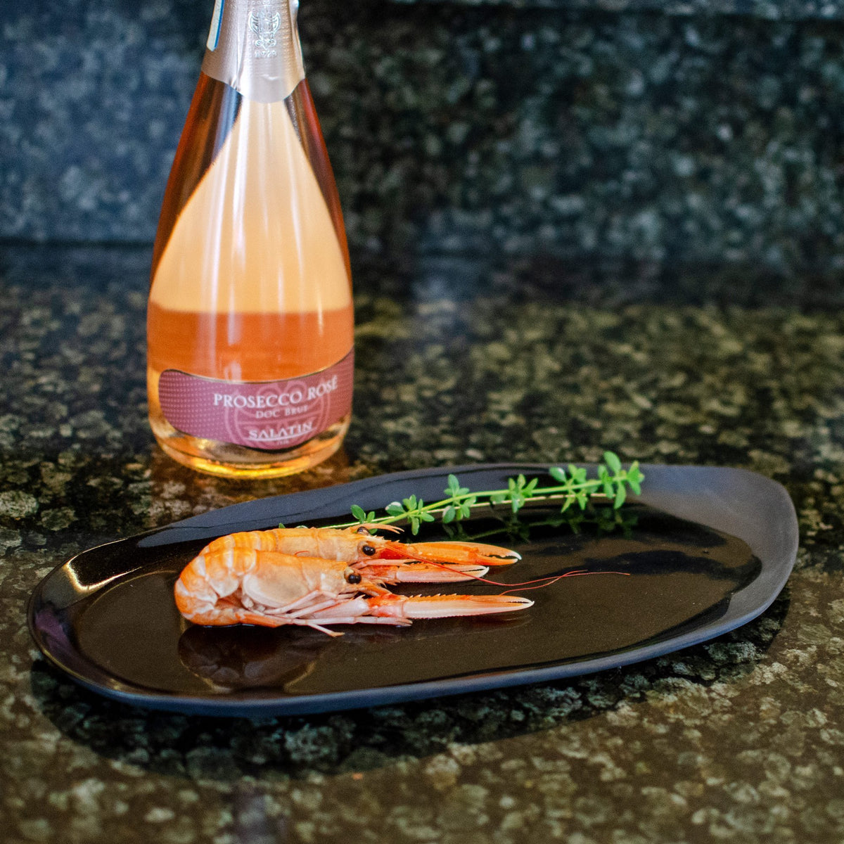 Food served on a black oval ceramic plate beside a bottle of rosé