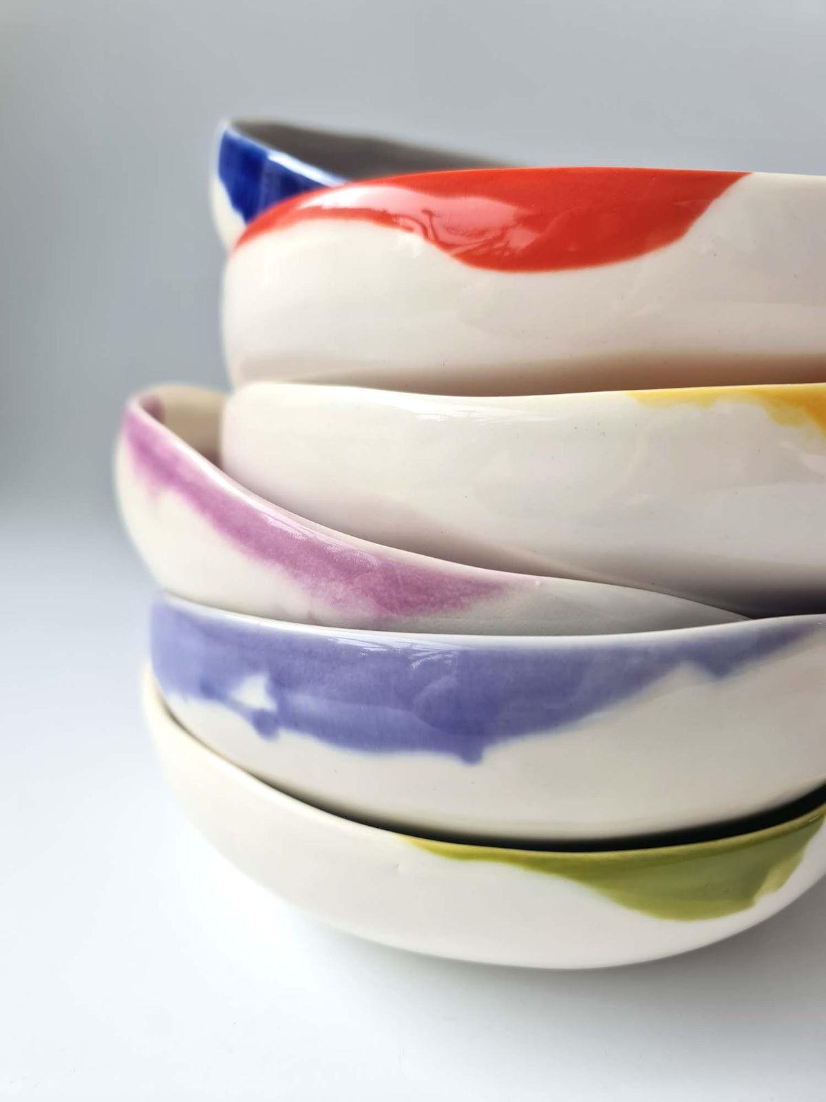 Stack of round ivory ceramic bowls with red, yellow, lavender, blue and green glazes