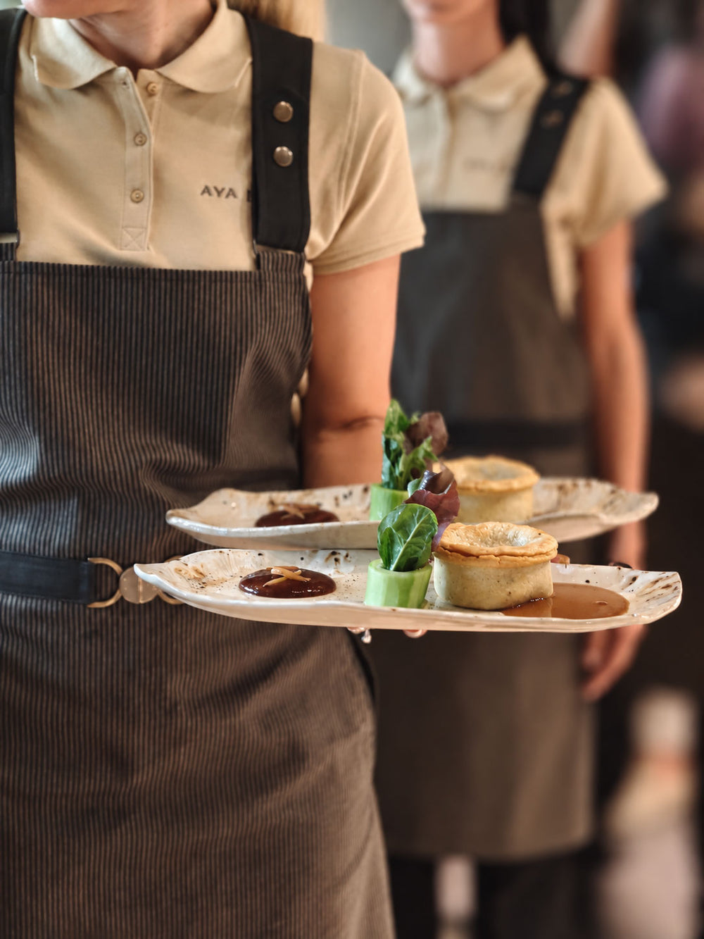 Waiter carrying custom restaurant plates with plated dishes, part of a tailored hospitality collection