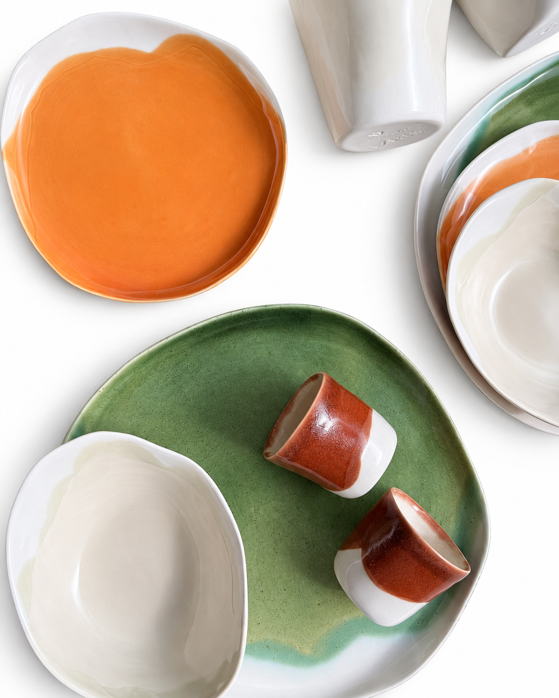 Close-up of olive-green, orange and ivory ceramic plates with terracotta espresso cups