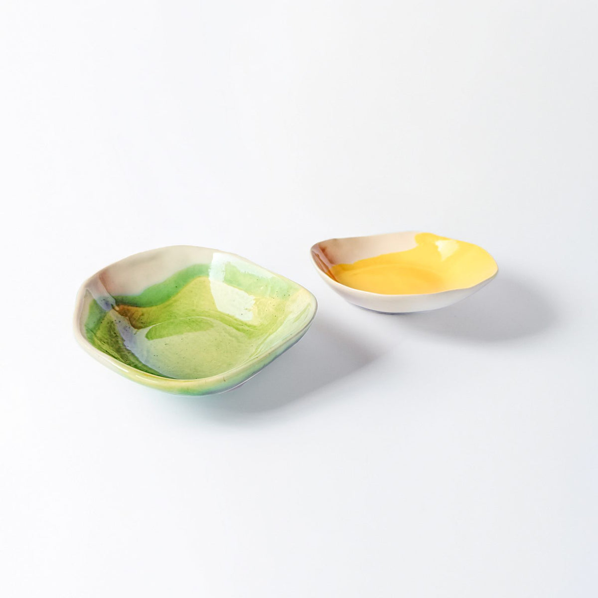 Two organic-shaped handmade dip bowls with green and yellow glaze on a white background