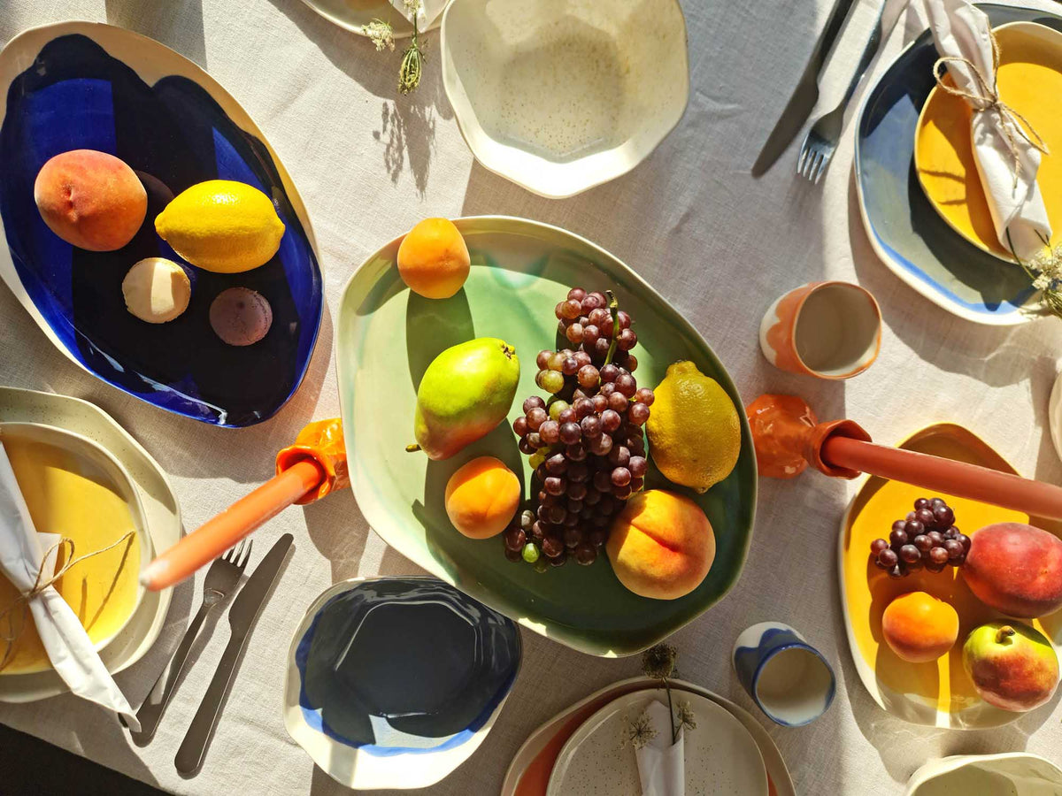 Table set with handmade ceramic plates and bowls in autumn glazes, filled with fruit