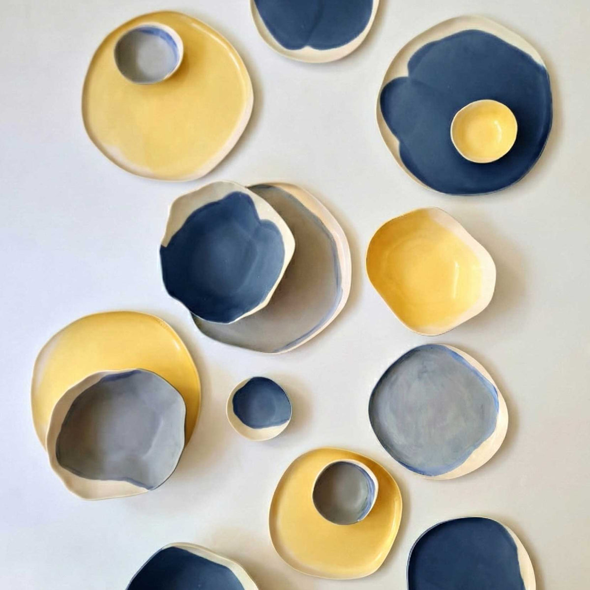Handmade plates, bowls and cups in denim blue and yellow glazes, arranged on white