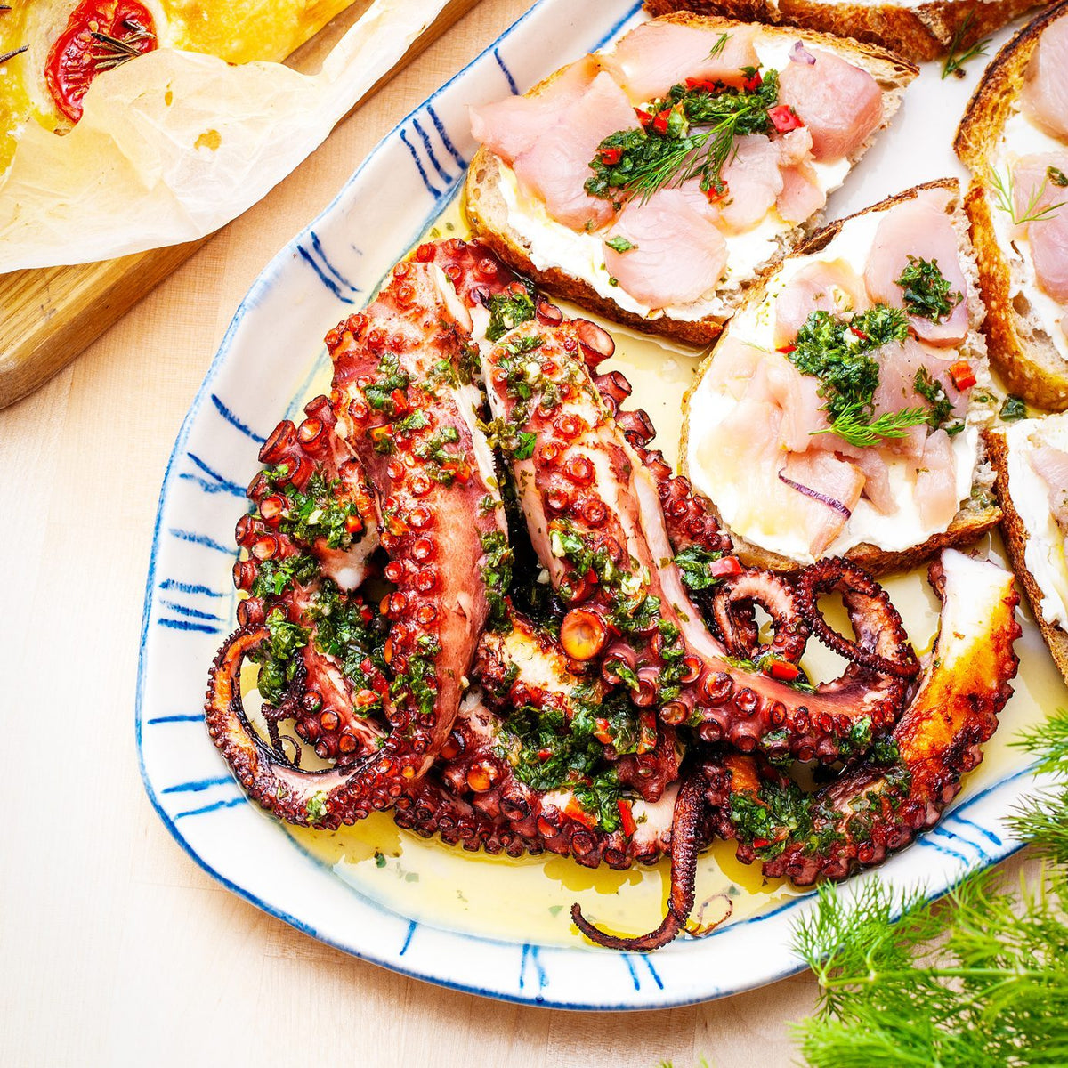 Grilled octopus and crudo toasts on an oval porcelain serving platter with Indigo brushstroke rim