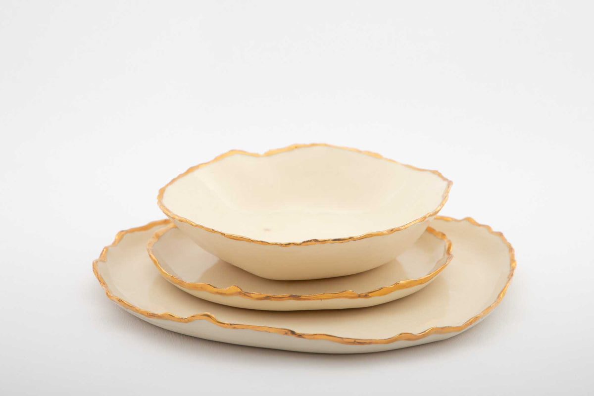 Side view of a Gilded Ridges bowl stacked on two ivory plates with gold rims