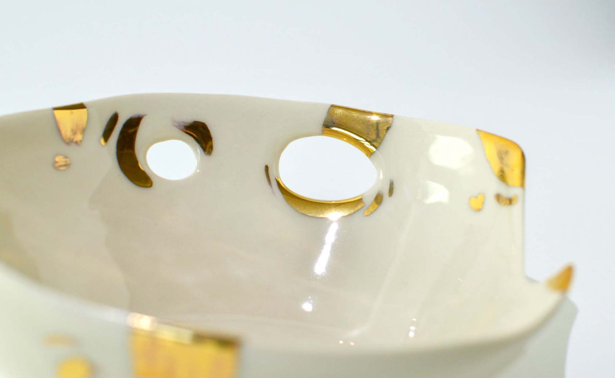 Close-up of a white porcelain bowl rim with pierced holes edged in gold, from the Laced collection