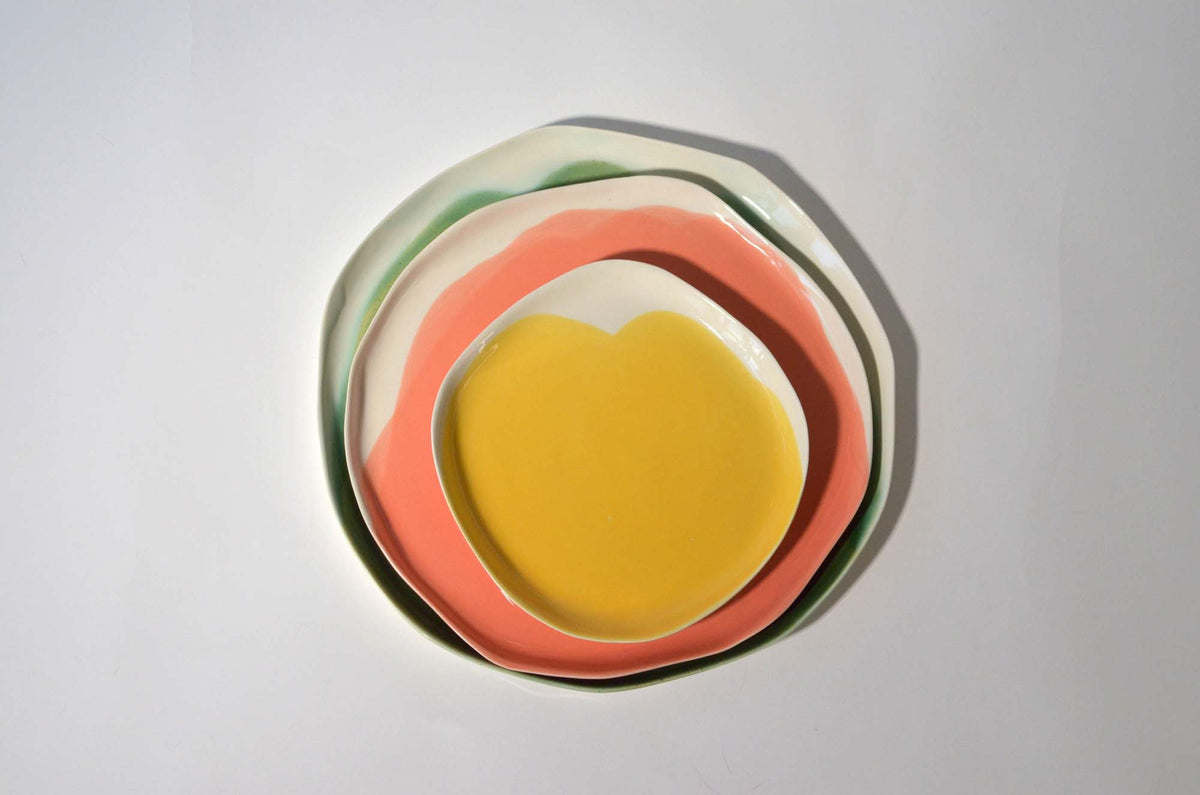 Three nested handmade plates in green, coral and yellow