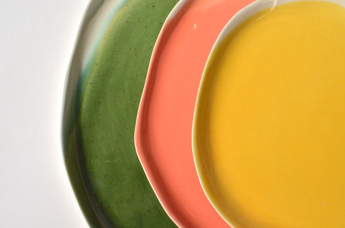Close-up of stacked green, coral and yellow handmade plates