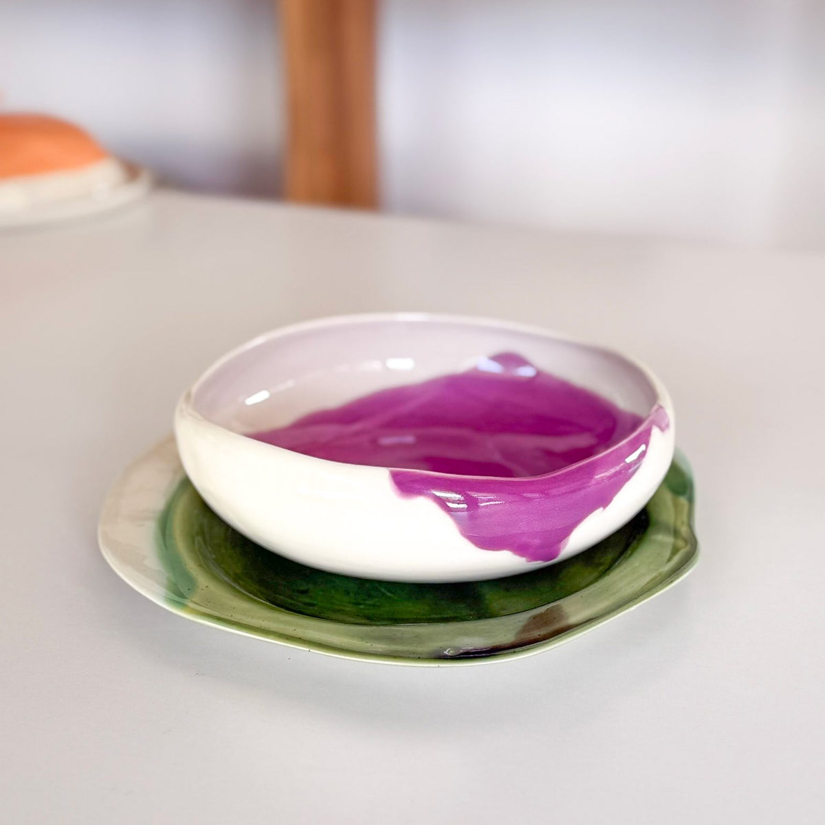 Ivory ceramic bowl with a flowing pink glaze inside, stacked on a green plate