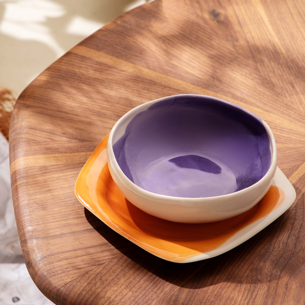 Purple ceramic bowl stacked on an orange plate and ivory plate