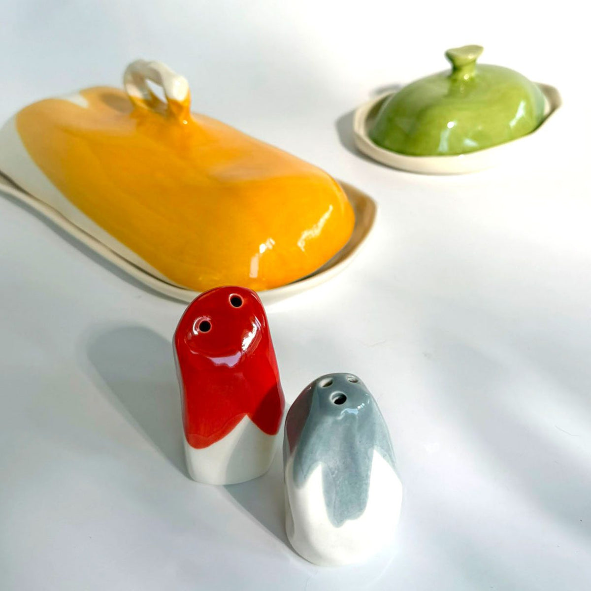 Red and blue ceramic salt and pepper shakers beside colourful lidded dishes