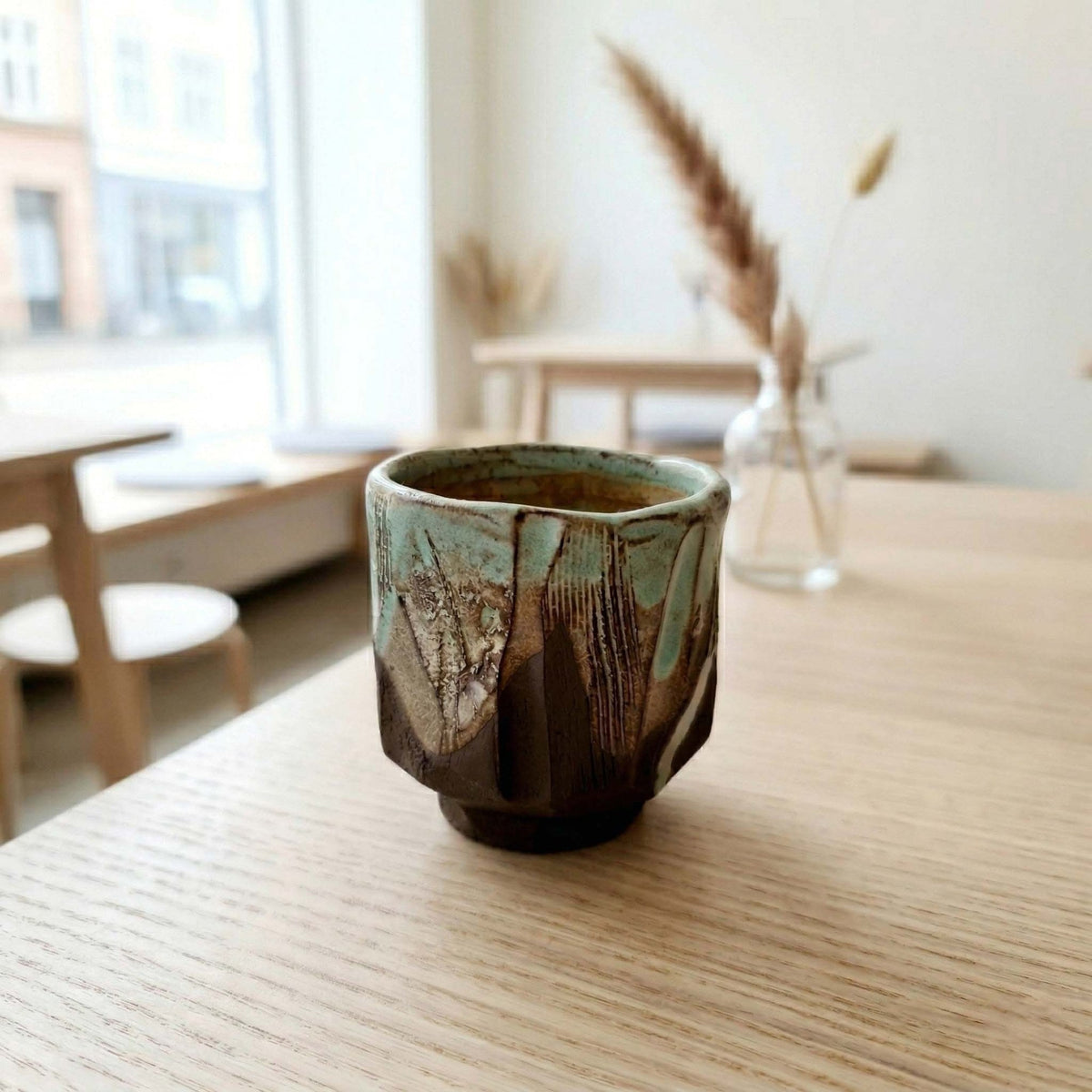 Handmade kurinuki espresso cup with green glaze on a café table