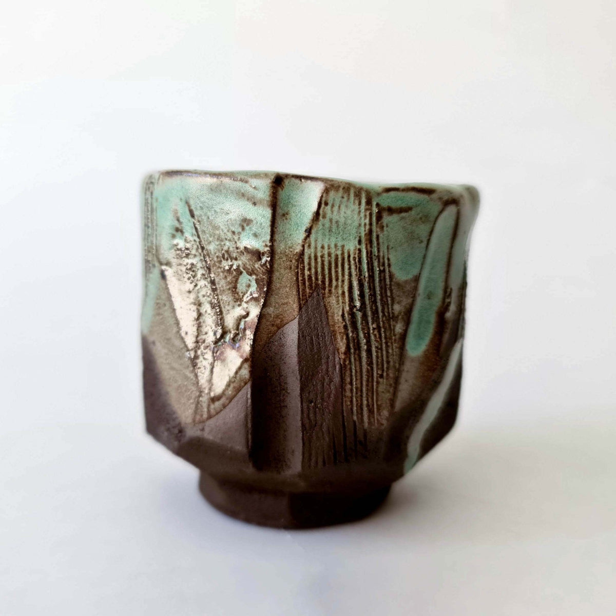 Close-up of a carved kurinuki coffee cup with green glaze and knife marks
