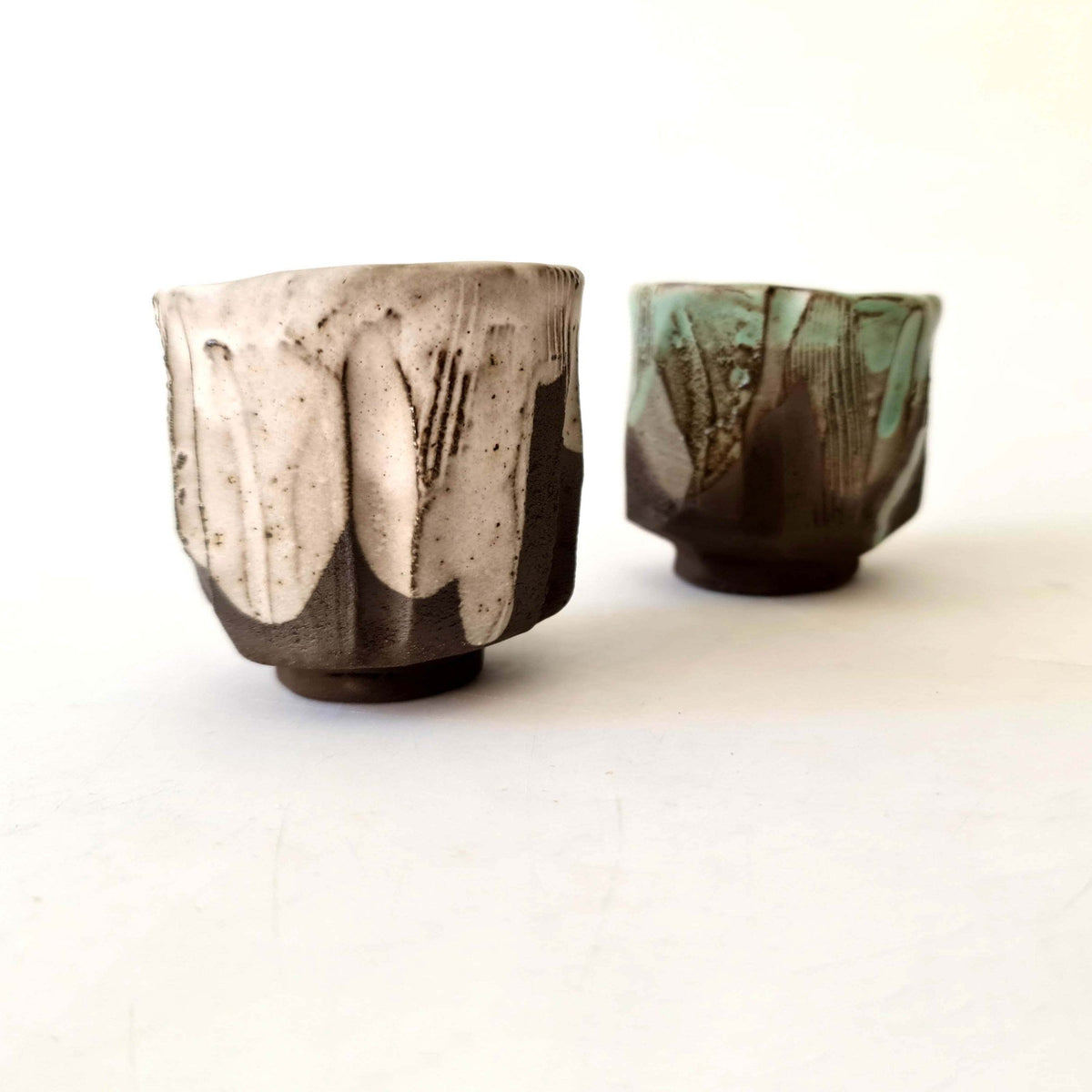 Two kurinuki coffee cups in cream and green glaze on dark clay