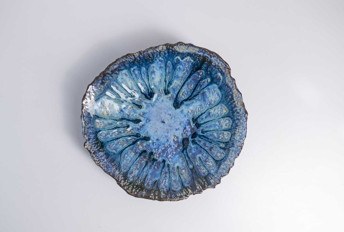Legged Plate from Black Clay from above, with blue reactive glaze pooling in radiating ridges