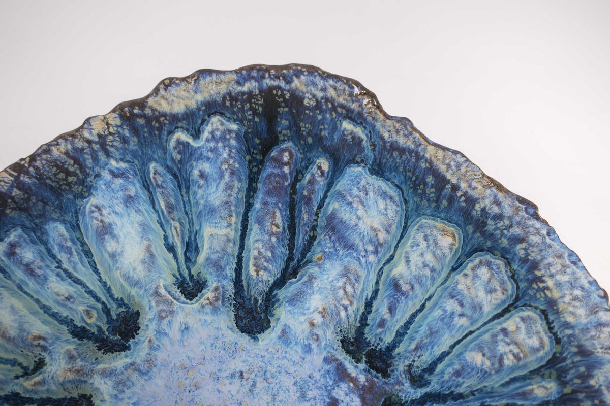 Close-up of the Legged Plate from Black Clay showing blue glaze flowing over carved ribs