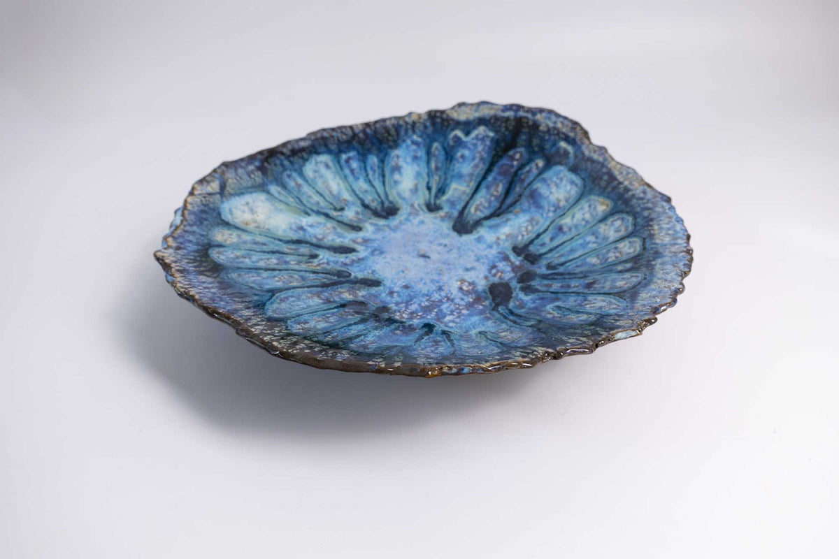 Legged Plate from Black Clay at an angle, deep blue glaze inside an irregular organic rim