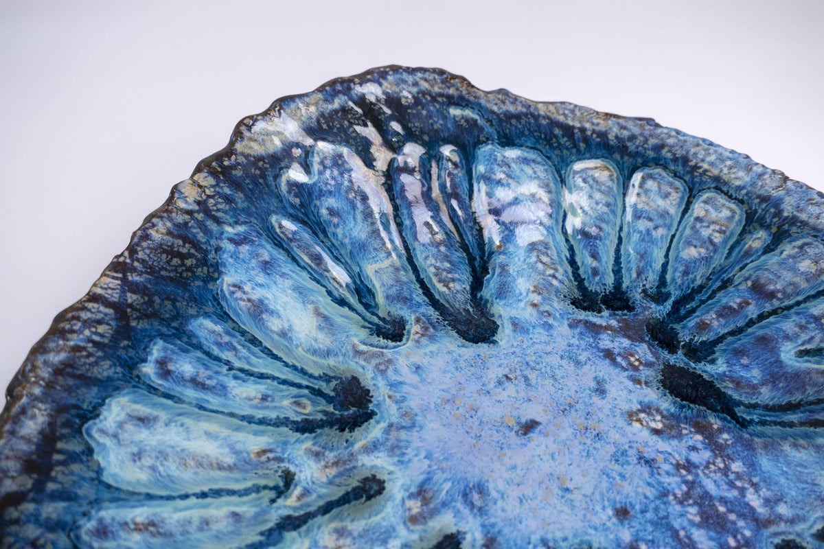 Detail of the ribbed rim on the Legged Plate from Black Clay with glossy blue and white glaze
