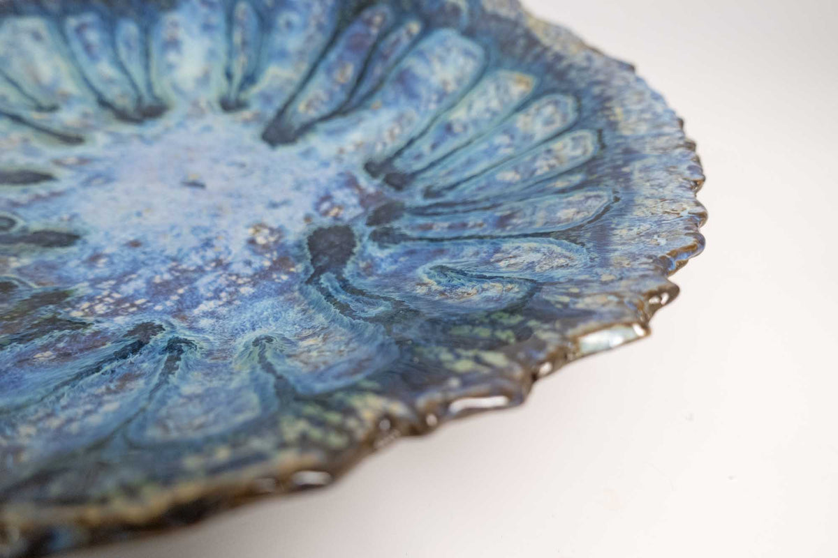 Angled close-up of the Legged Plate from Black Clay with violet-blue glaze and textured edge