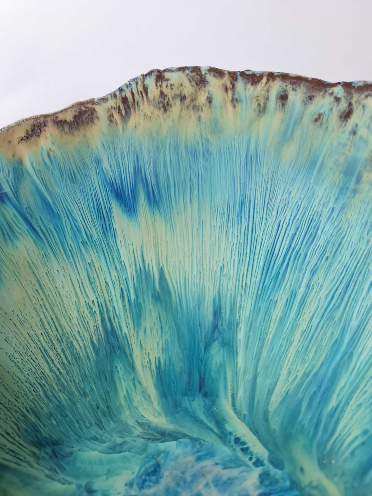 Close-up of turquoise and cream glaze streaks radiating across a Legged Plate from Black Clay