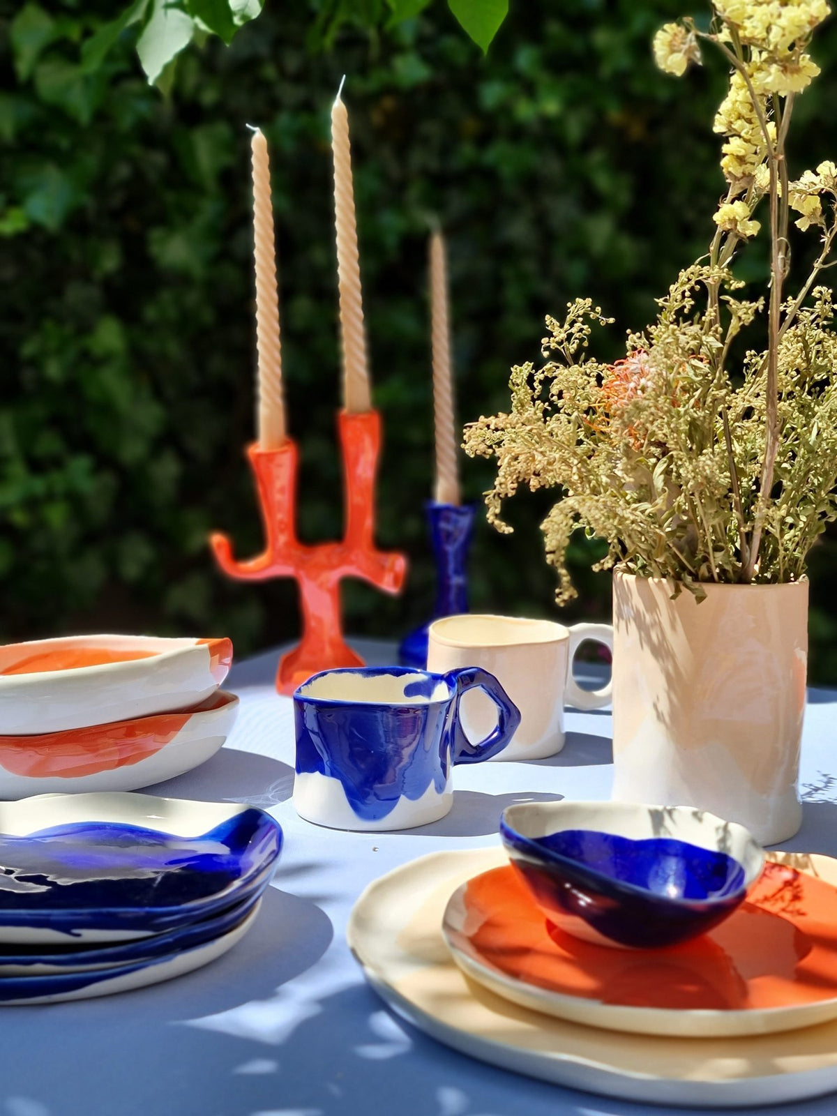 Colourful ceramic tableware and mugs with tall candles on an outdoor dining table