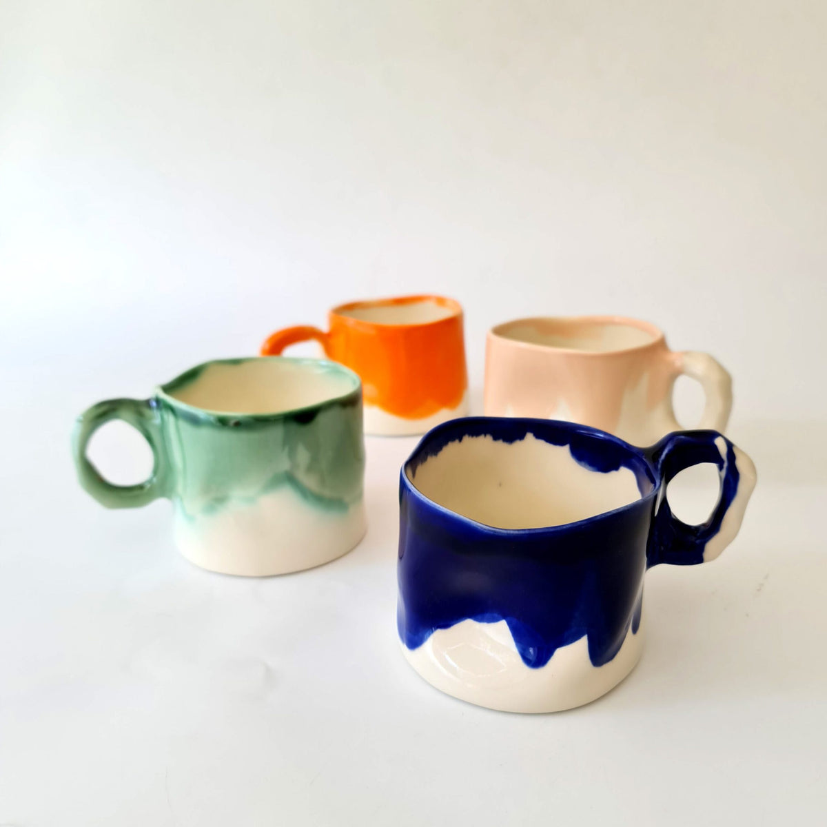 Four handmade mugs in orange, green, pale pink and royal blue glazes