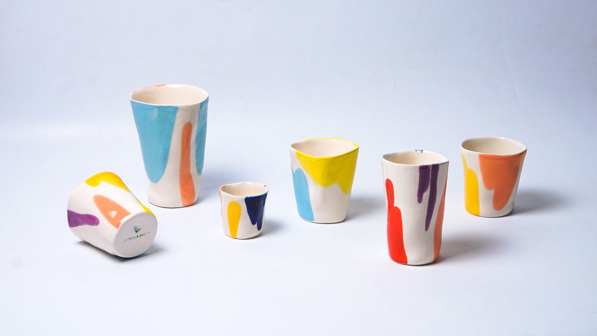 Handmade multicolour coffee cups and a matching jug arranged on white