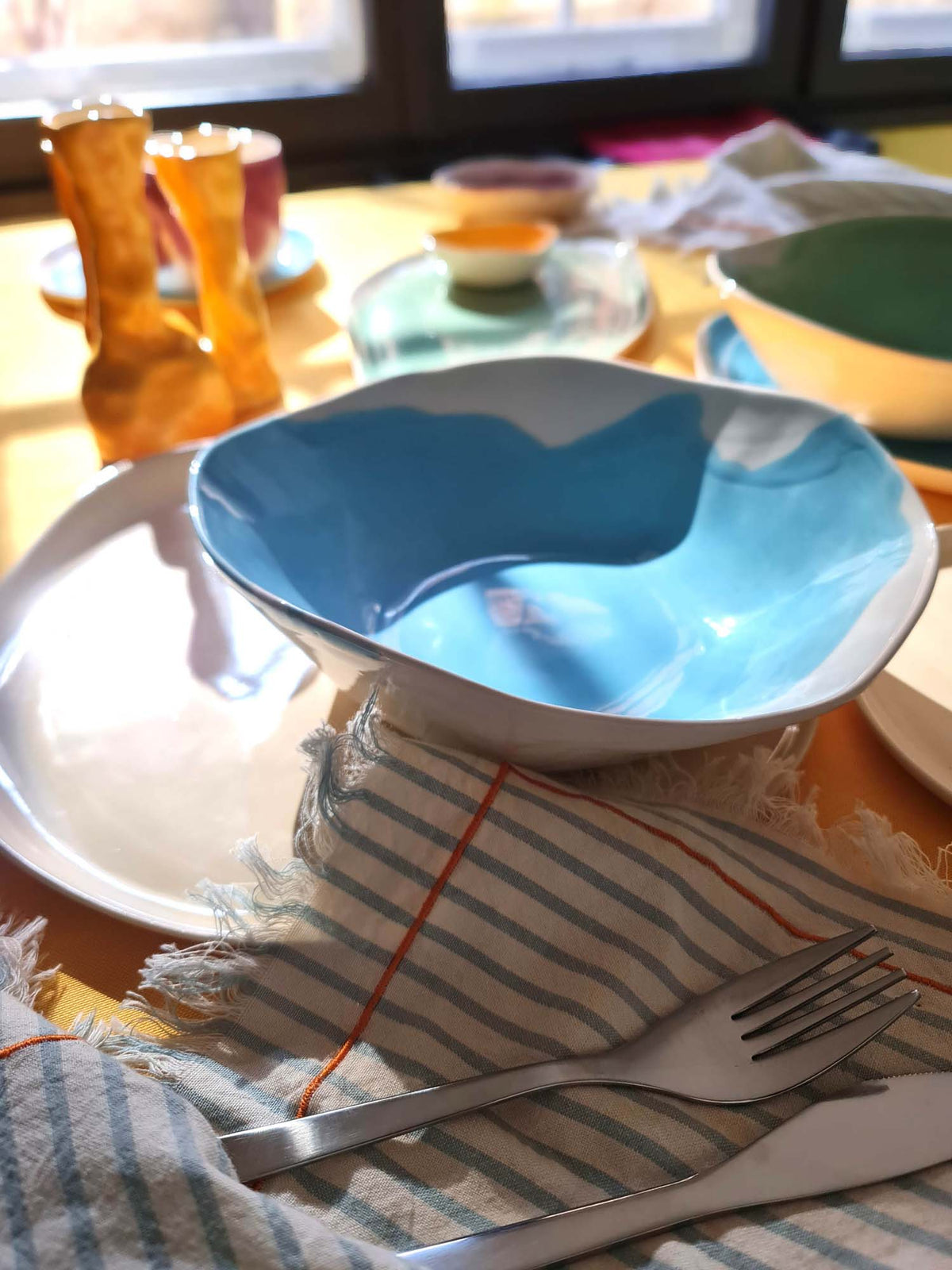 Sky-blue handmade ceramic bowl on a dining table beside colourful cups