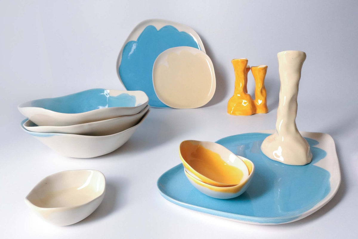 Handmade blue and yellow plates, bowls, cups and a candleholder arranged on white