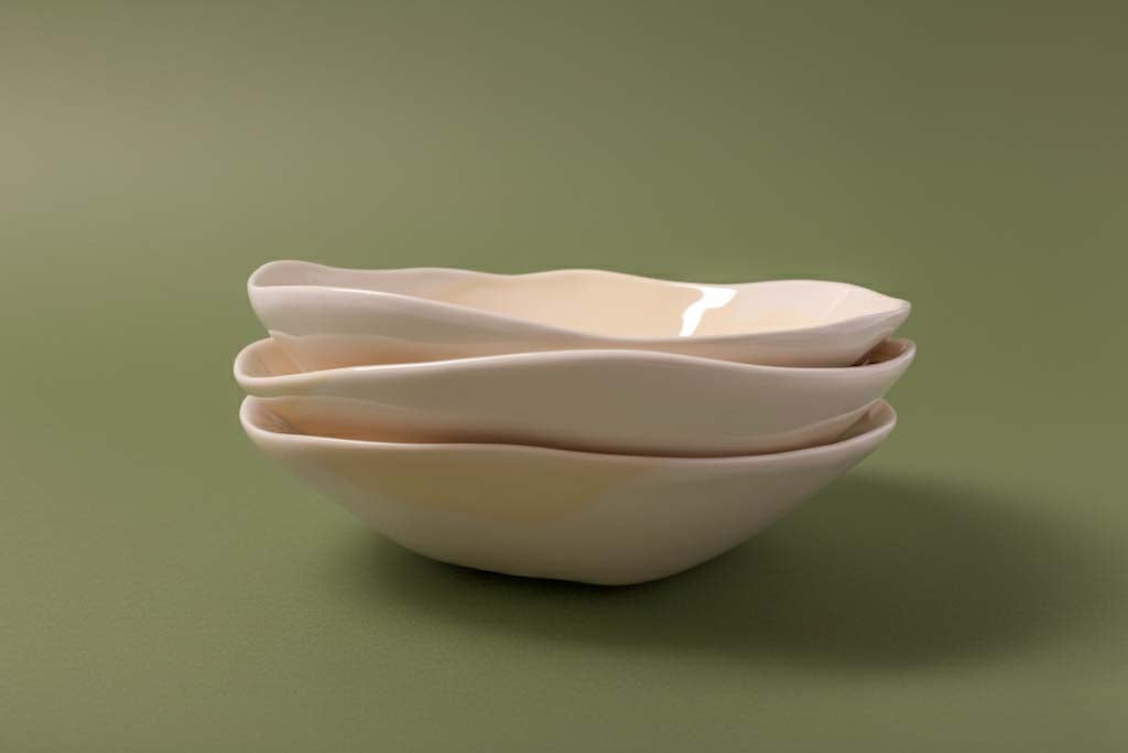 Three nested ivory handmade ceramic bowls on a green background