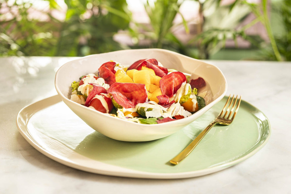 Handmade ceramic bowl with salad, placed on a pale-green plate outdoors