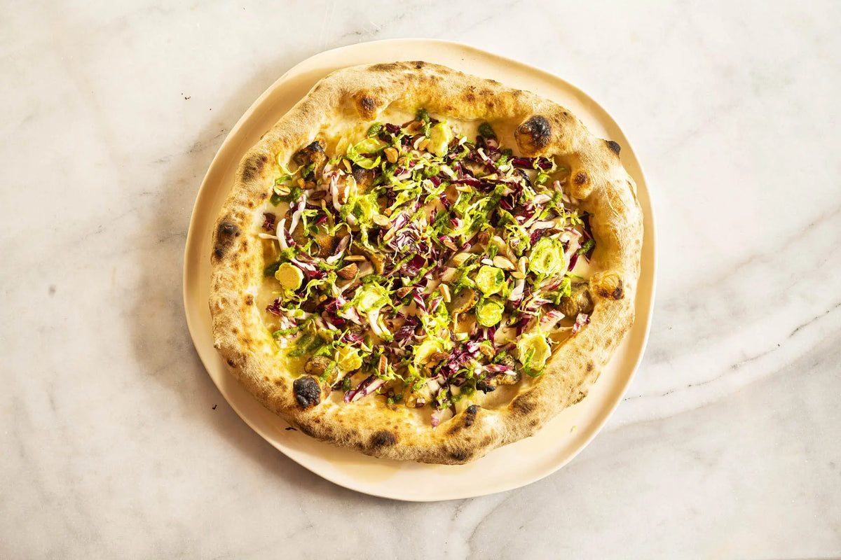 Pizza with leafy toppings on a handmade ivory ceramic plate