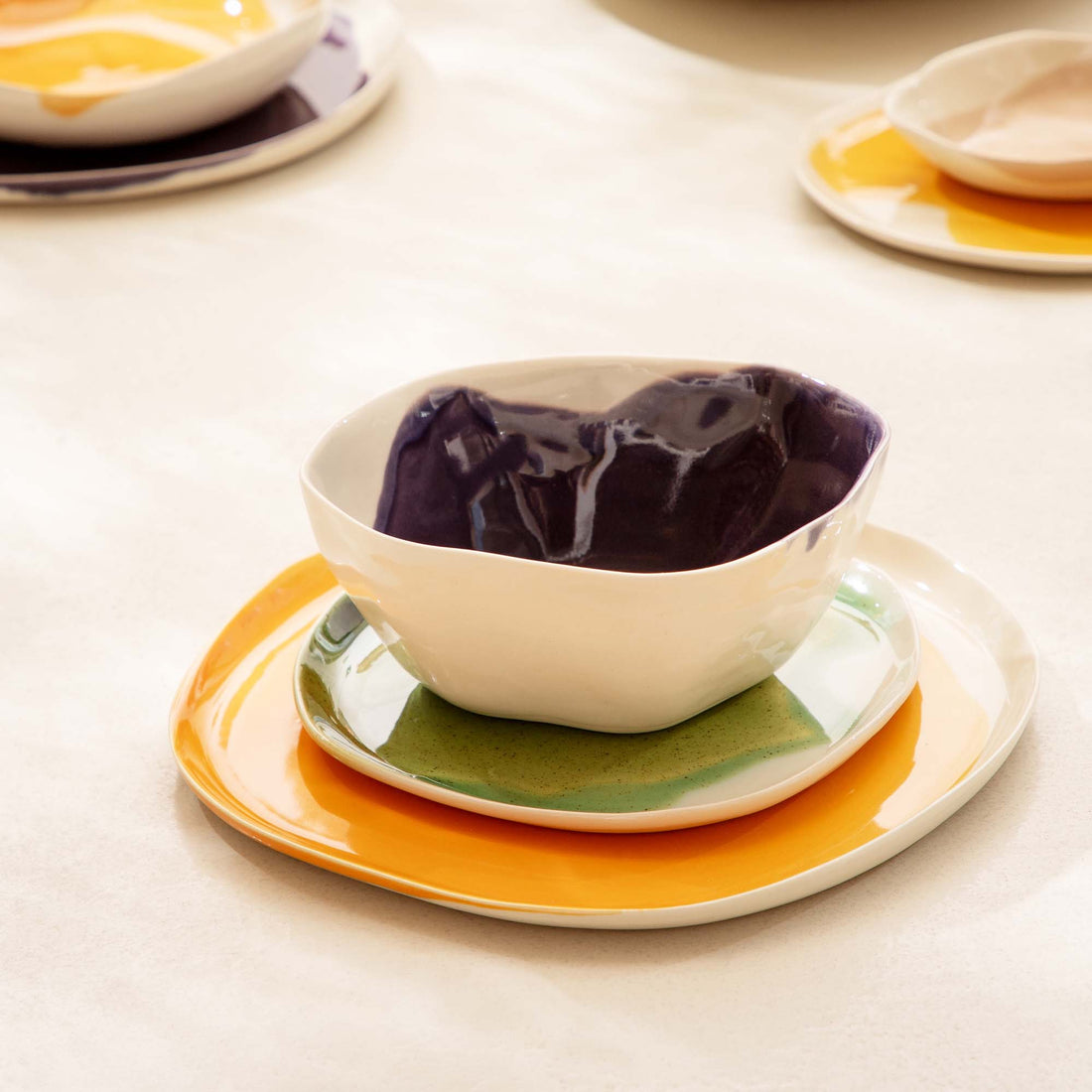 Purple glazed bowl on stacked yellow and green plates in a place setting