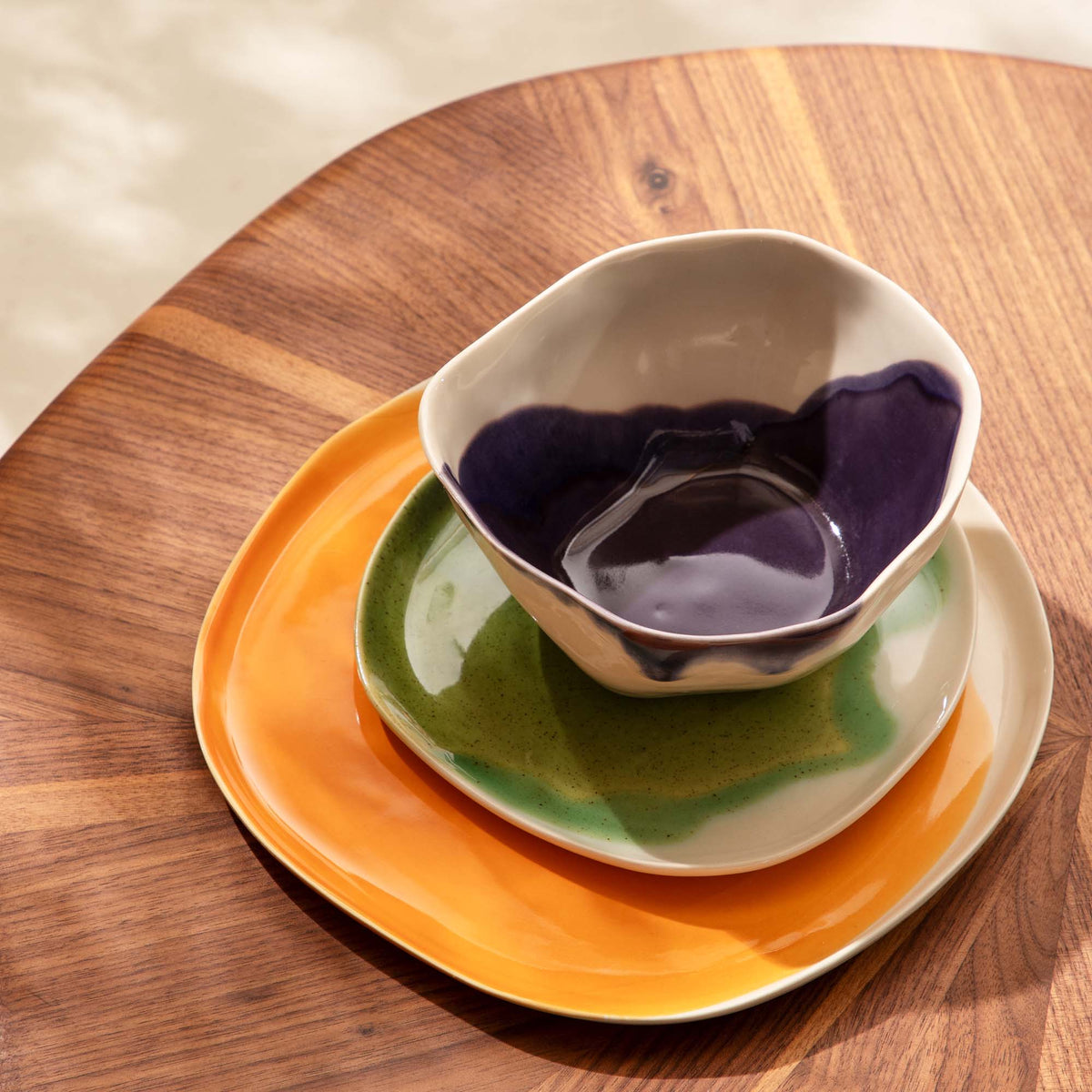 Handmade 3-piece dining set: purple and white bowl on a green side plate and an orange dinner plate, on a wooden table