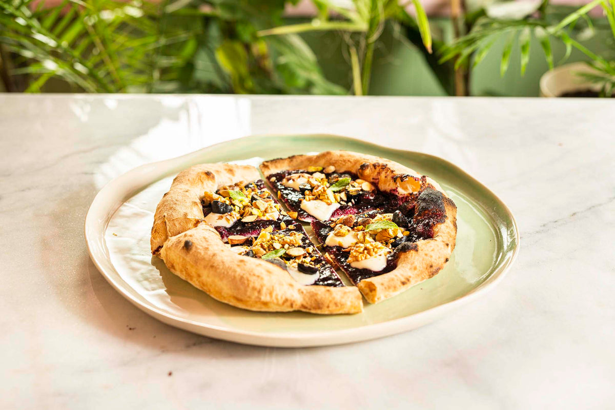 Pizza on a pale green handmade ceramic plate beside a drinking glass