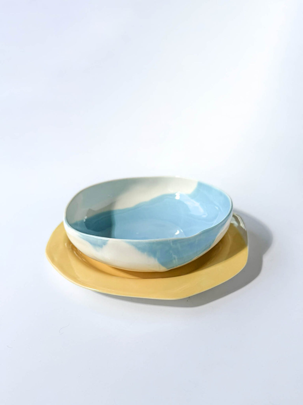 Sky-blue ceramic bowl stacked on a yellow handmade plate